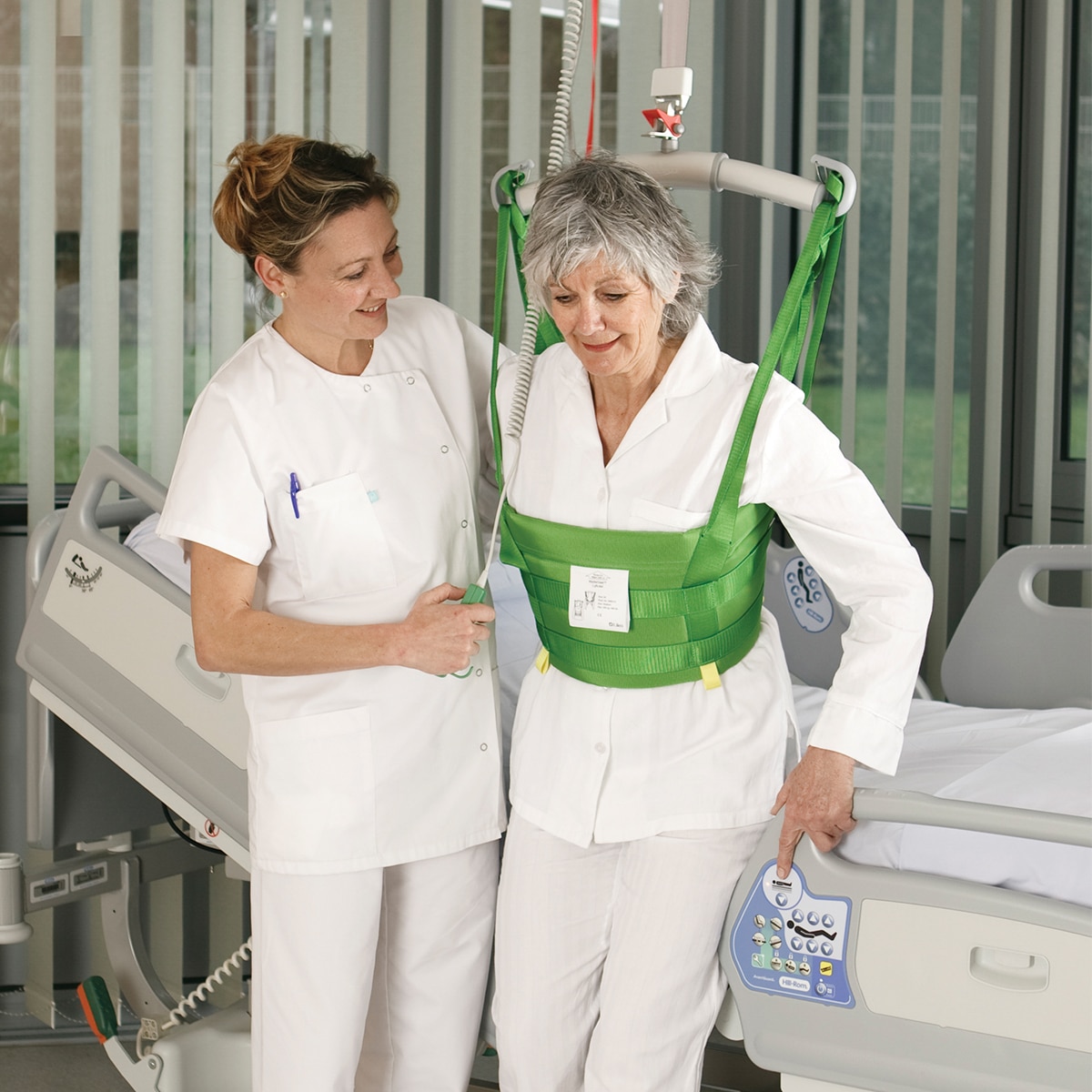 Een arts helpt een patiënt in een ziekenhuiskamer te lopen met een Hillrom-plafondlift en MasterVest